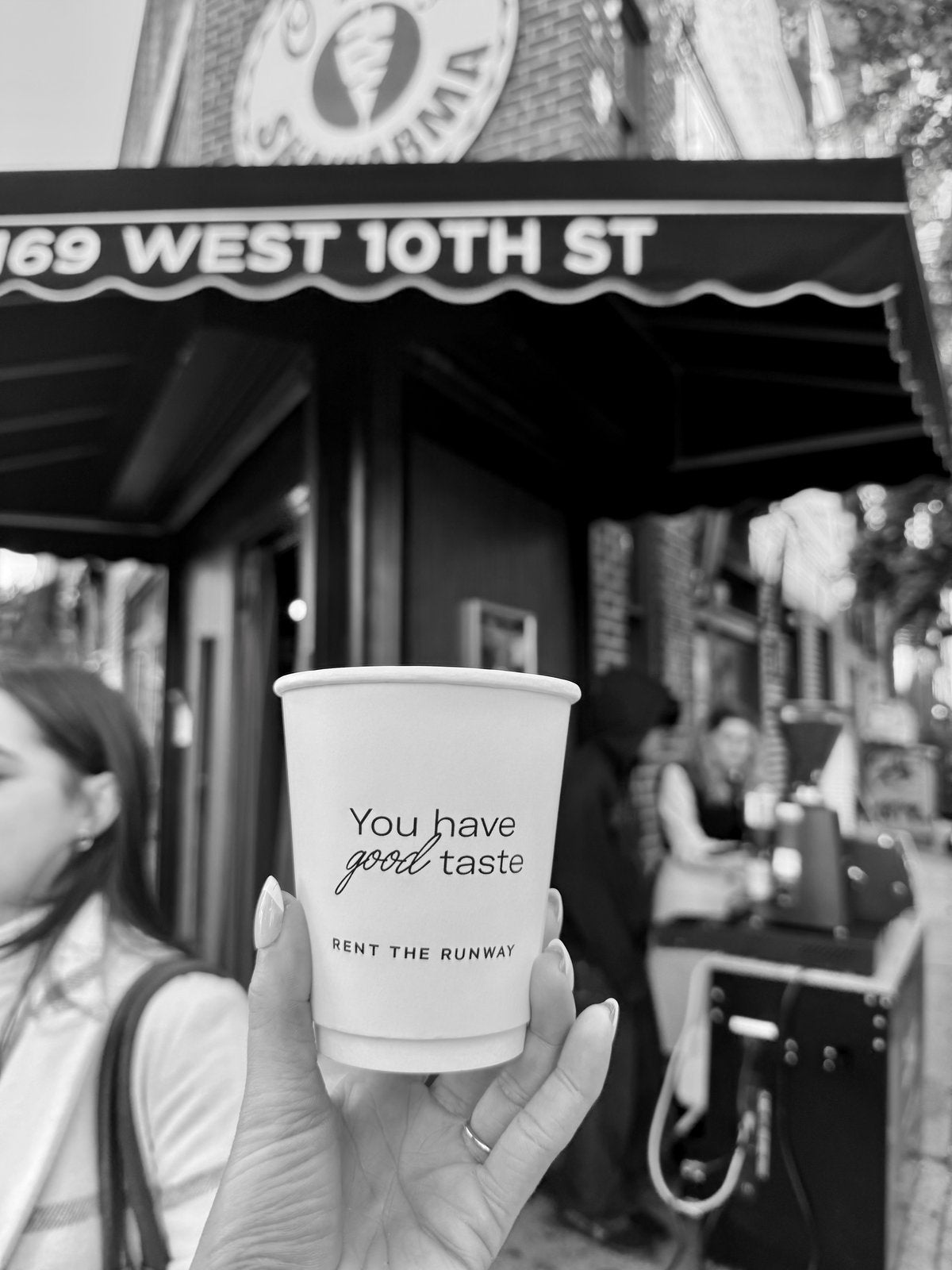 Rent the Runway 'You have good taste' cup held in front of 169 West 10th St