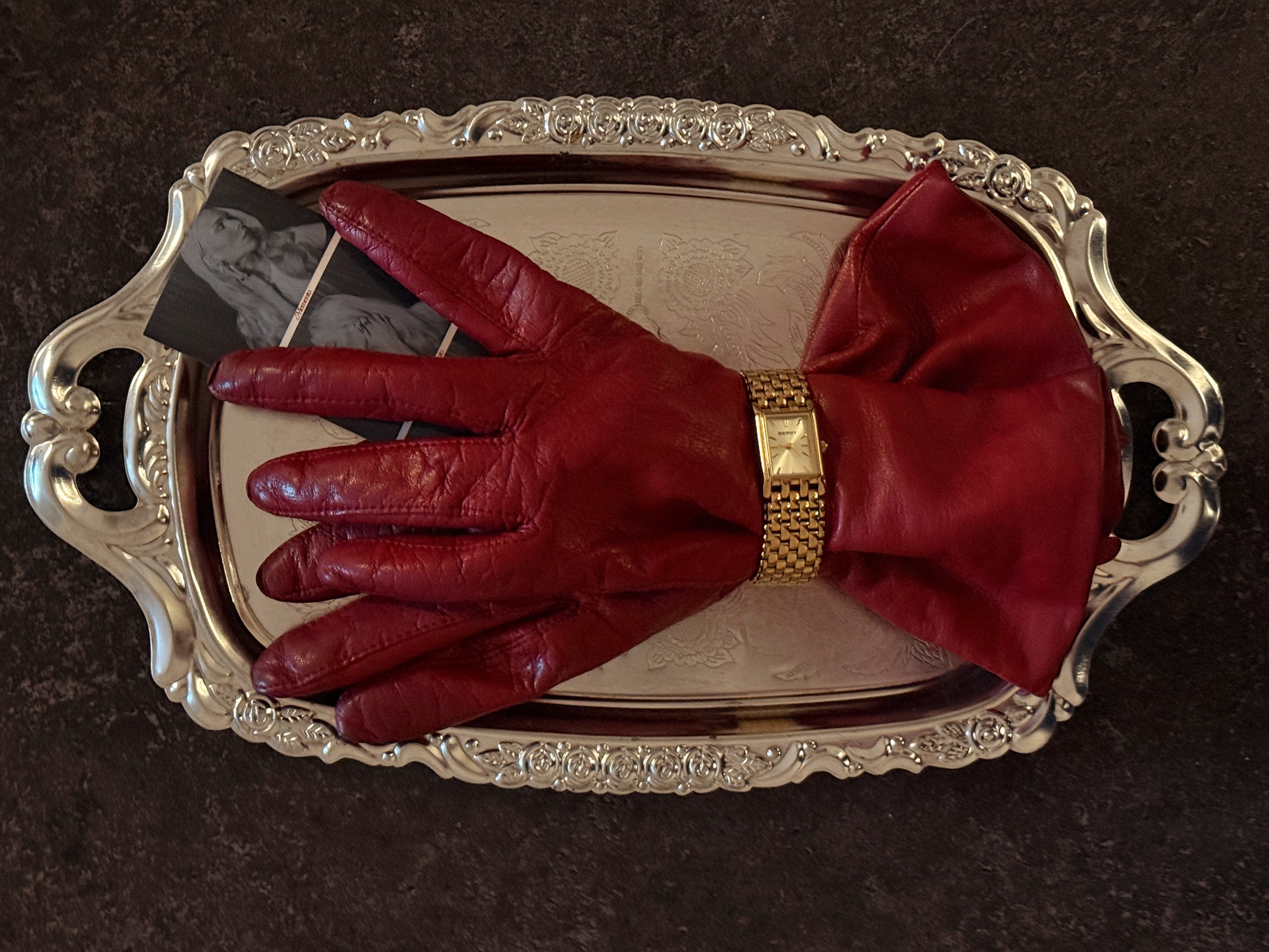 Burgundy leather glove with gold watch on an ornate silver tray, Memento photo tucked between fingers