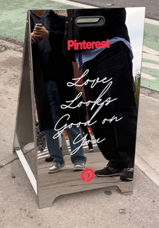 A mirrored sidewalk sign from a brand activation reading Love Looks Good on You.