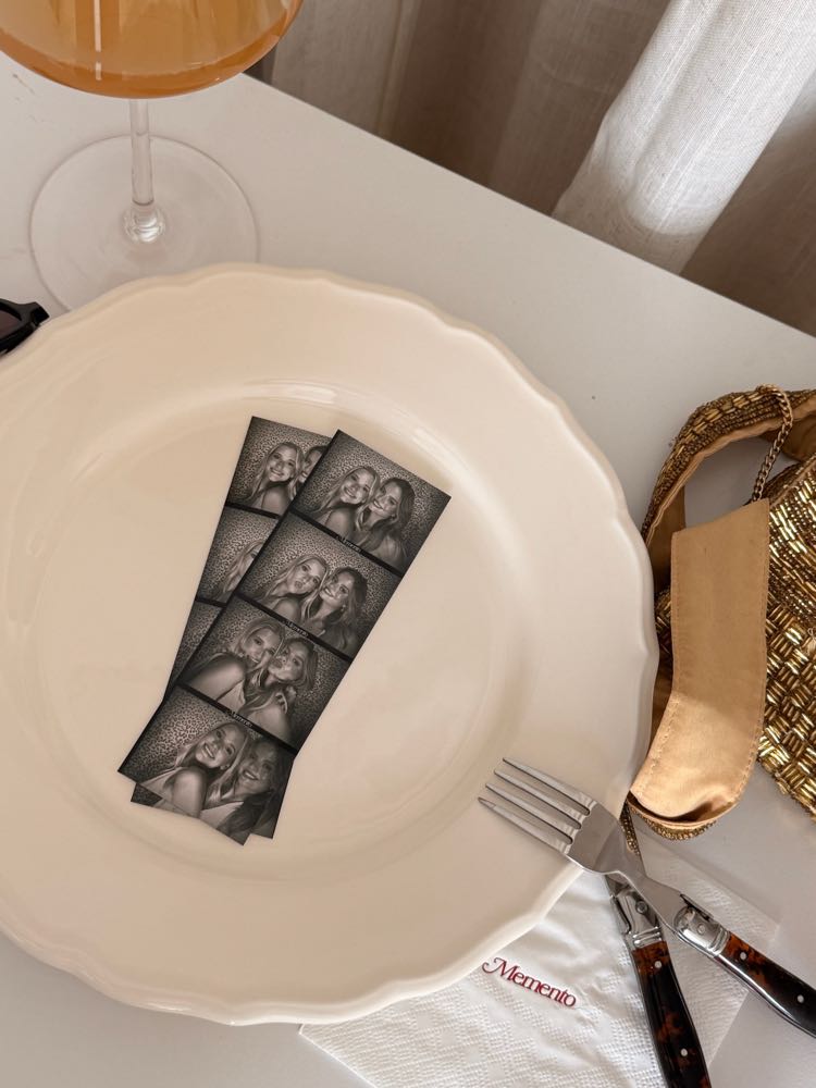 Two Memento photo strips on a scalloped plate beside a glass of wine.